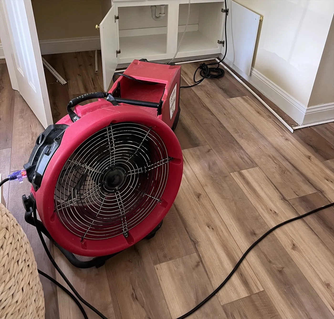 Red air mover and dehumidifier running on a laminate floor beside an open bathroom vanity