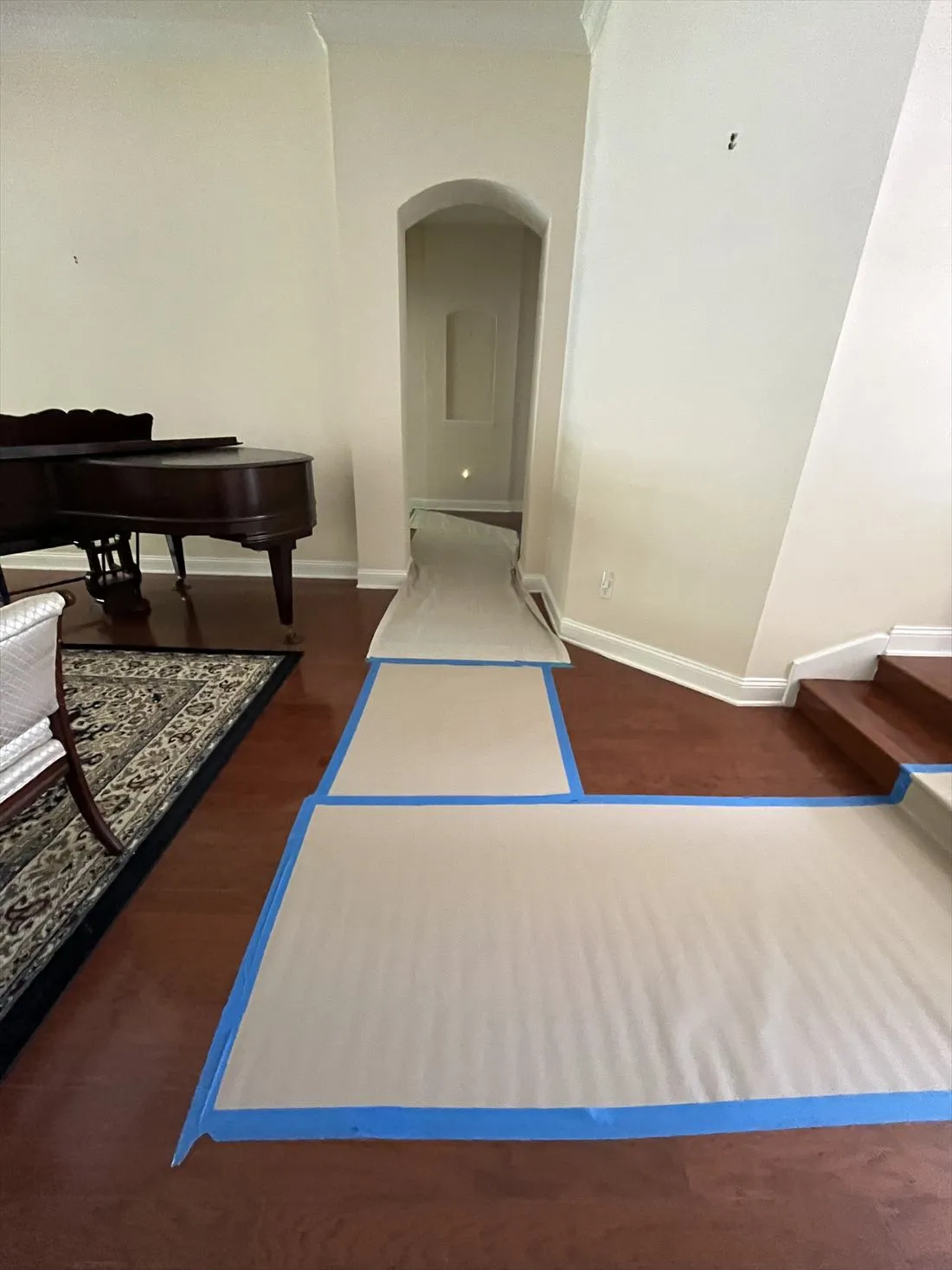 Floor protection paper taped down across a wood floor and through an archway past a grand piano