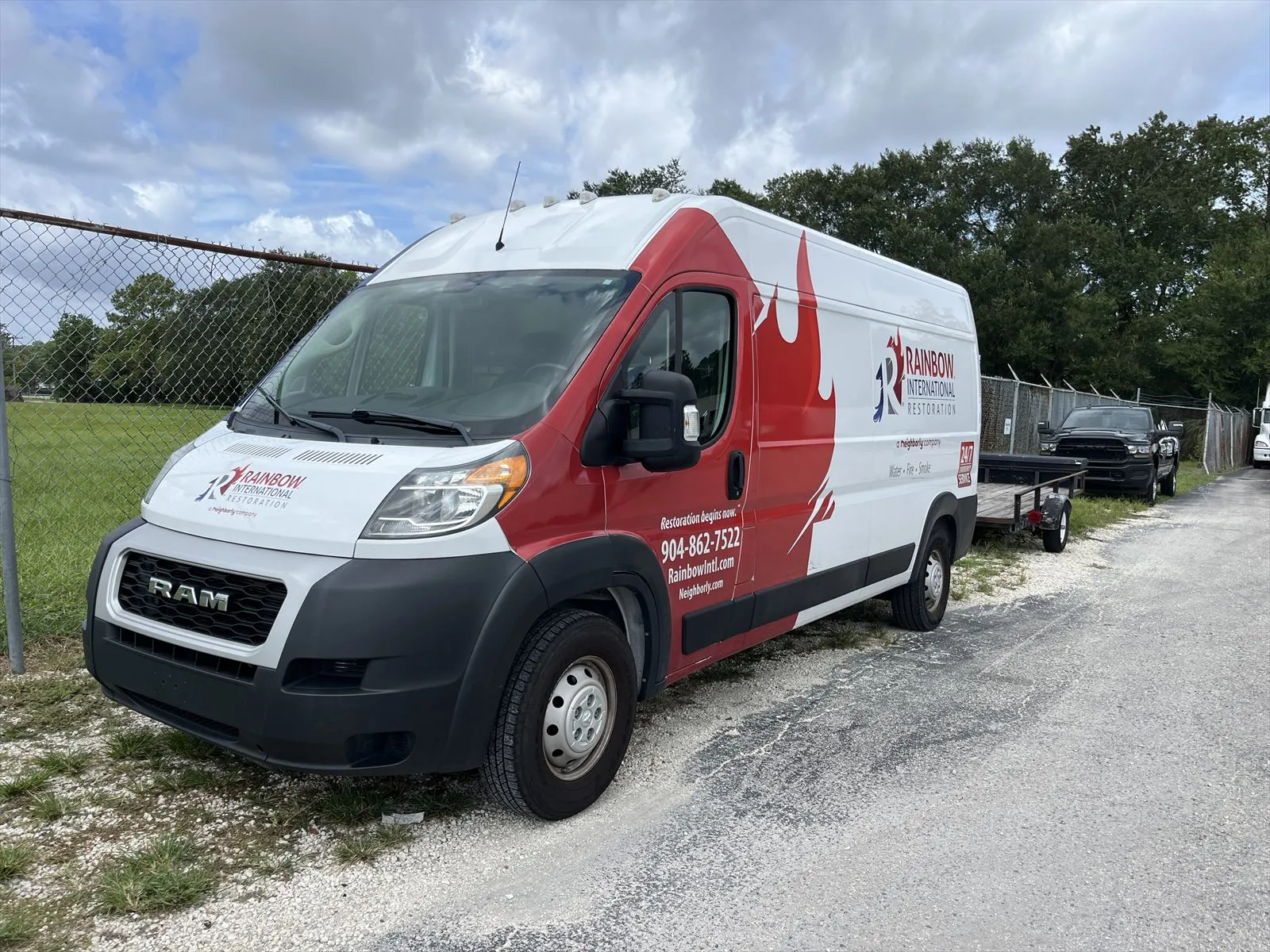 Red and white Rainbow service van parked beside a fence