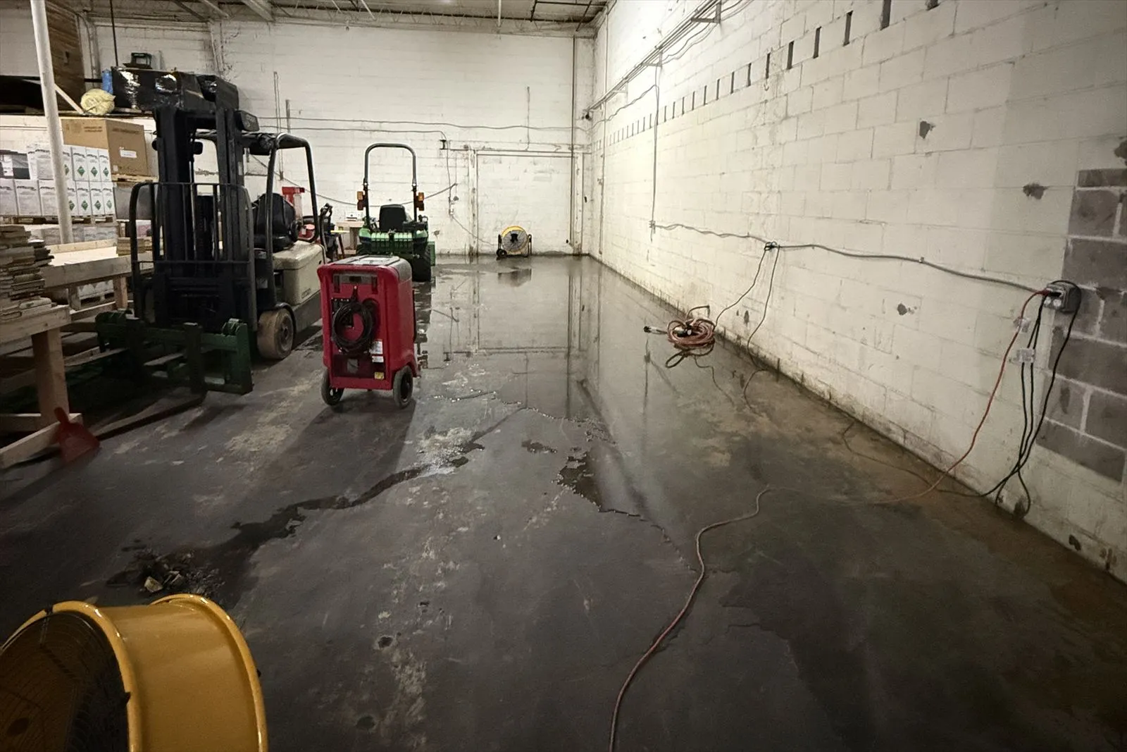 Flooded concrete floor in a warehouse with a red dehumidifier and yellow air movers running